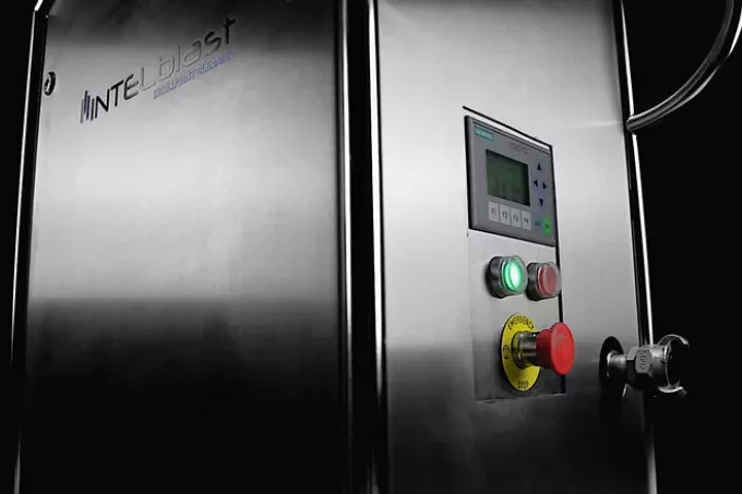 Zbliżenie panelu maszyny przemysłowej ze stali nierdzewnej z logo INTEGblast, ekranem wyświetlacza, przyciskami, w tym zielonym i czerwonym, wyłącznikiem awaryjnym, idealnym do wynajmu urządzeń do czyszczenia takim lodem.